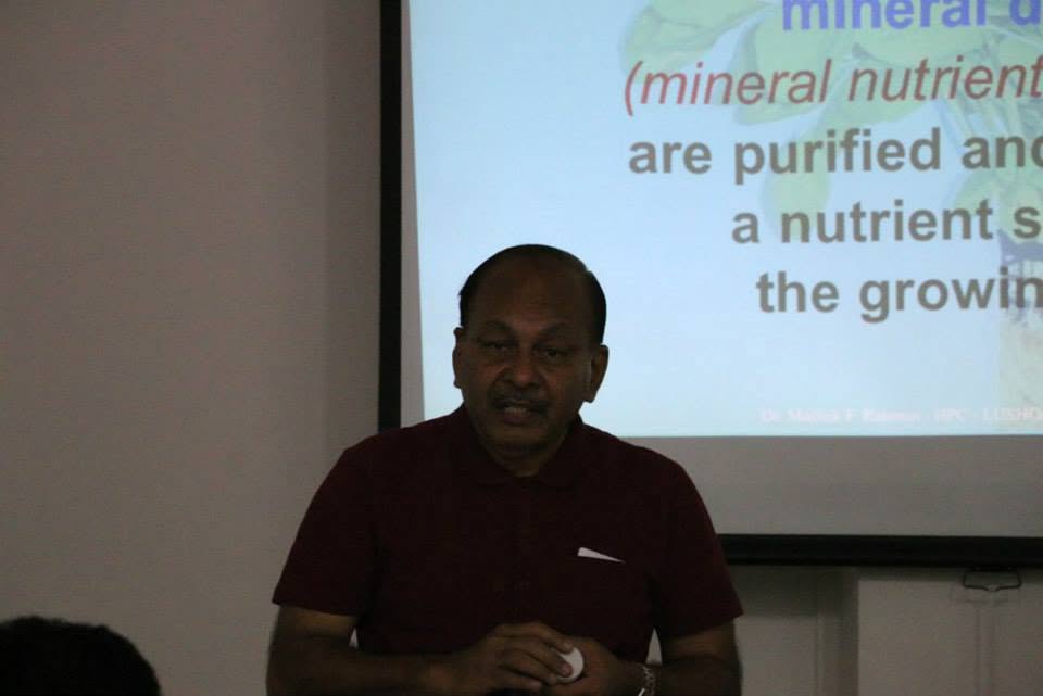 Portrait of Dr Mallick speaking to the class in front of a projected slide about mineral nutrients being purified into a nutrient solution