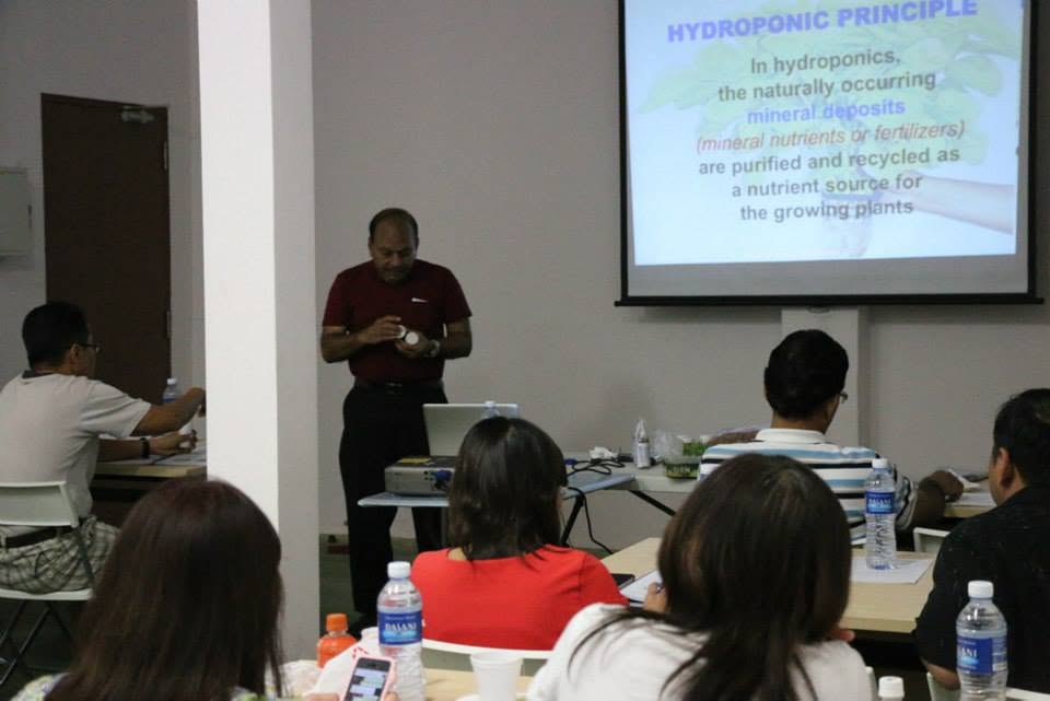 Dr Mallick teaching in front of a projected slide headed Hydroponic Principle, explaining that naturally occurring mineral nutrients are purified and recycled as a nutrient source for growing plants