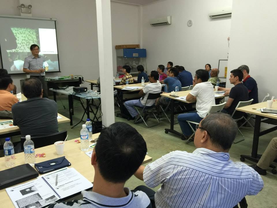 Wide view of the full classroom during the session, participants seated at tables with their kits while the trainer teaches at the front