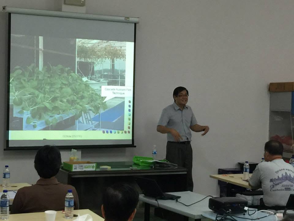 Geoffrey Chow standing beside a projected slide showing a cascade nutrient film technique system, teaching the seated class