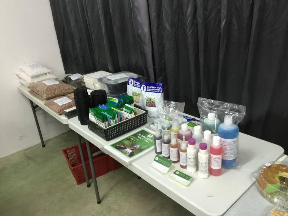 A supply table laid out with nutrient concentrate bottles, pH solutions, seed packets, net pots, clay pebbles and other growing media