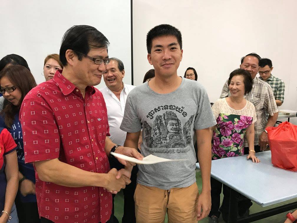 A participant shaking hands with the trainer while receiving his course certificate, with classmates smiling around them