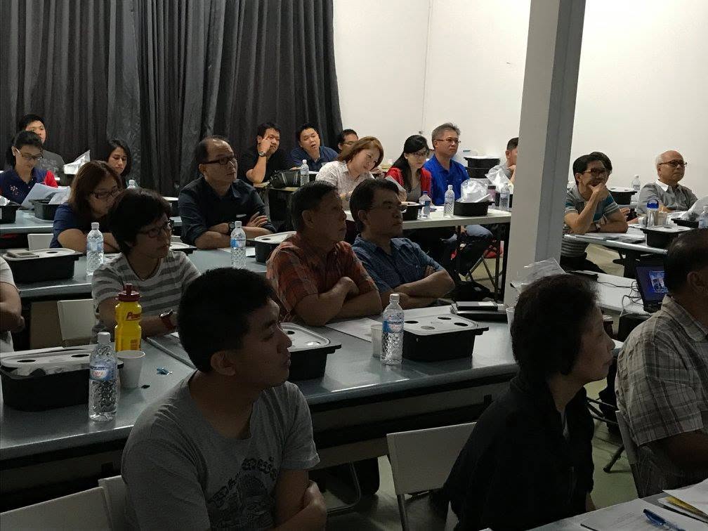 A full classroom of participants seated at tables listening during the hydroponics session, kits and notes in front of them