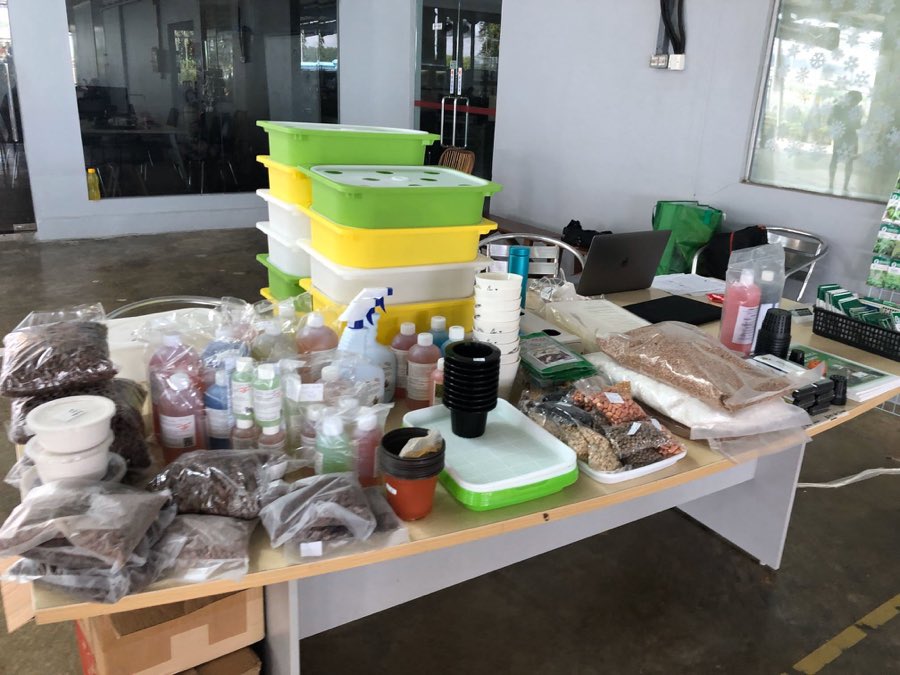 A table laid out with hydroponics starter kits, stacked grow tubs with lids, nutrient bottles, net pots, clay pebbles, seeds and growing media
