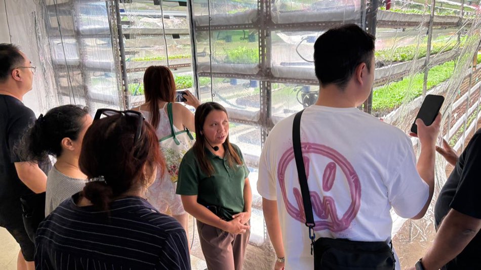 A farm guide in a green polo with a headset explaining the growing system to class participants beside a plastic-curtained growing area