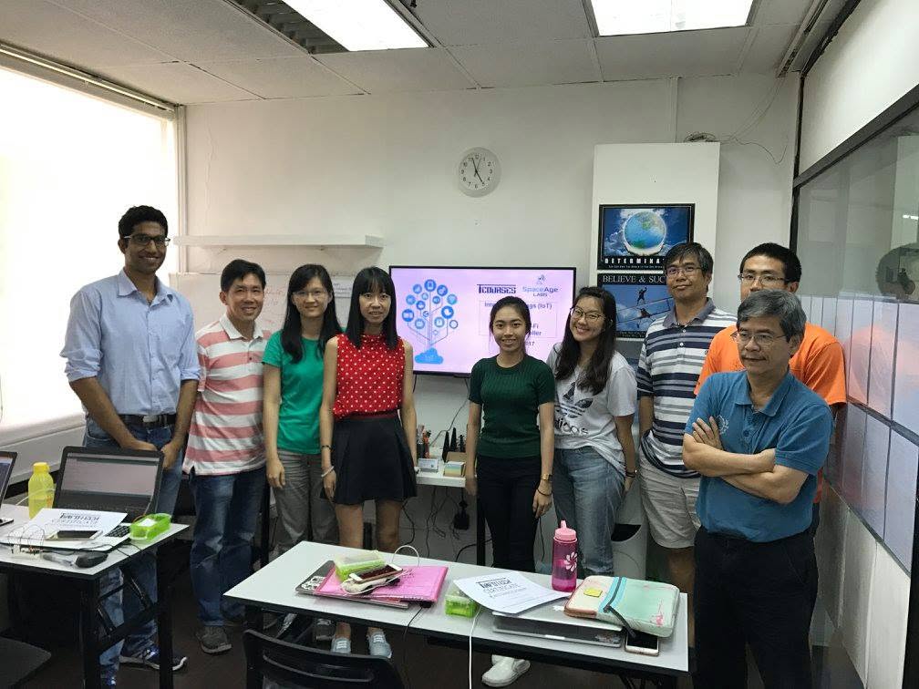 The 7 April 2017 Internet of Things class posing for a group photograph with trainer Mr Deepak at Bukit Timah Shopping Centre, the IoT title slide on the screen behind them