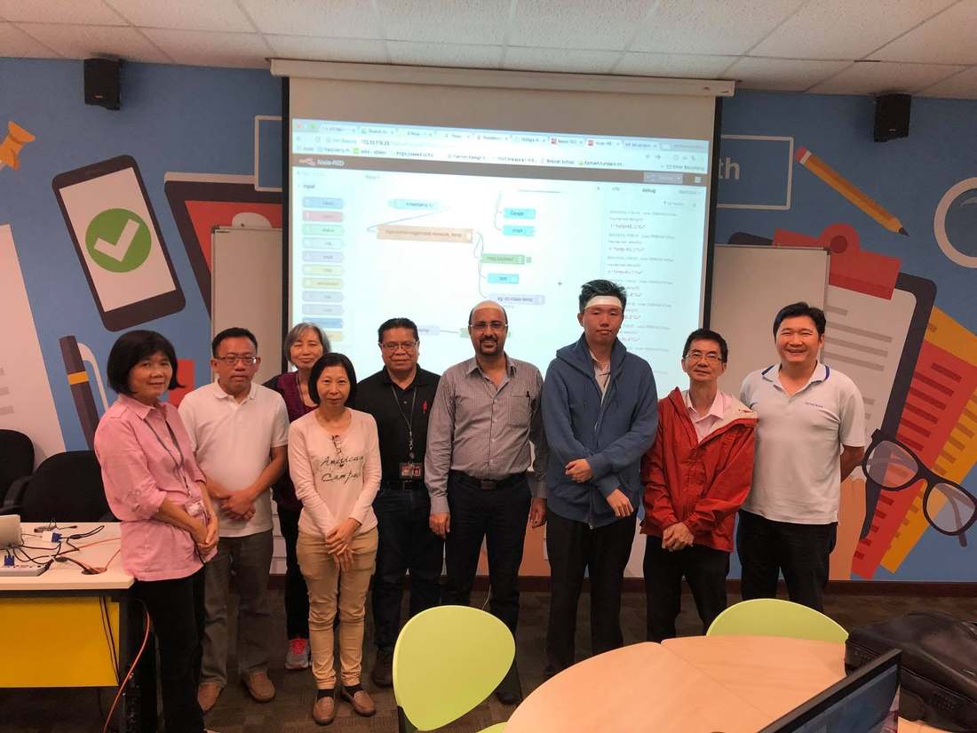 ITE College West staff and trainer Mr Reza posing together in front of a projector screen showing a Node-RED flow at the 3 January 2018 IoT class