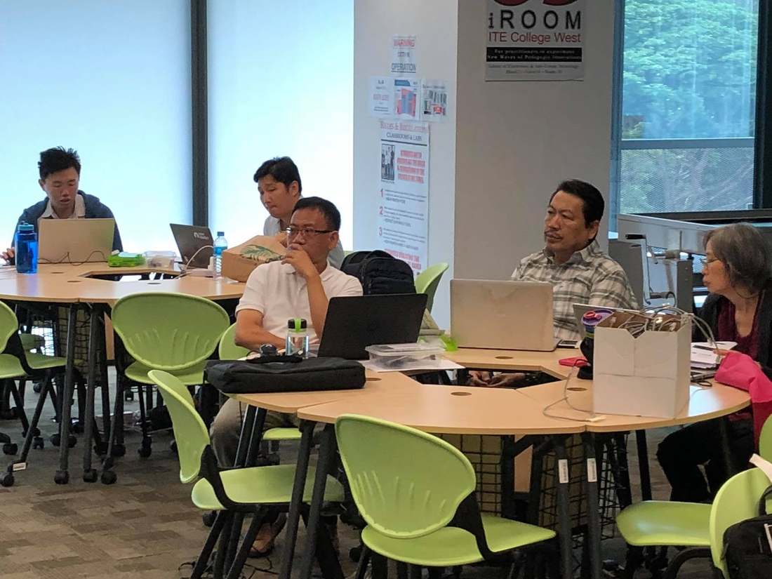 ITE College West staff seated at round tables with laptops during the IoT class, an iROOM ITE College West banner visible on the wall behind them
