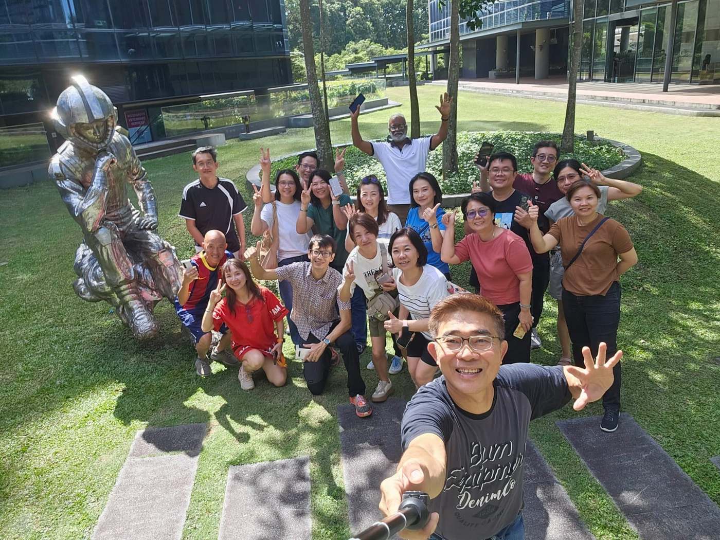 The 21 December 2025 mobile photography class posing outdoors on a lawn beside a chrome astronaut sculpture, phones in hand