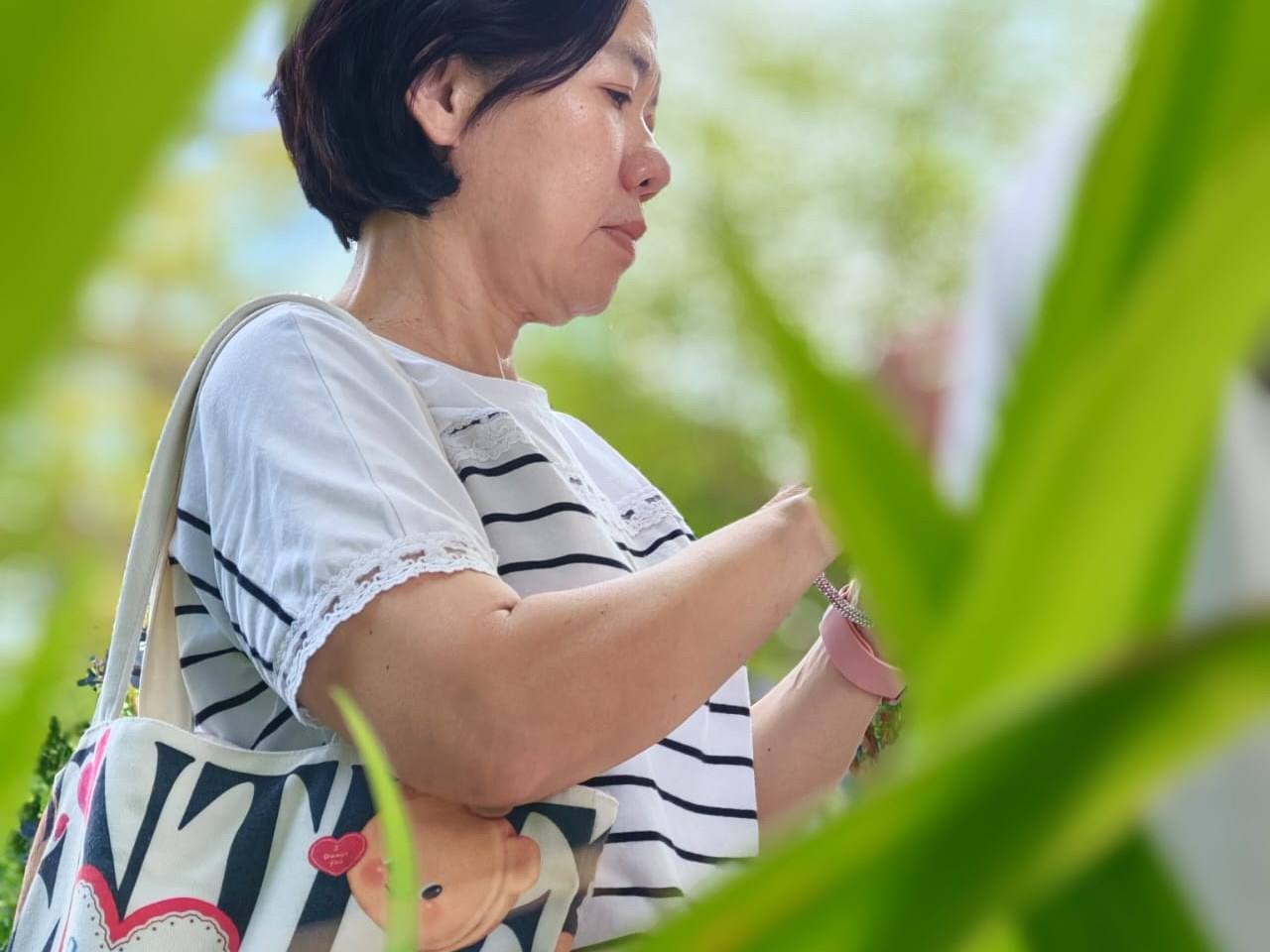 Candid portrait of a learner photographed through blurred green leaves, shot on a smartphone during the outdoor practical