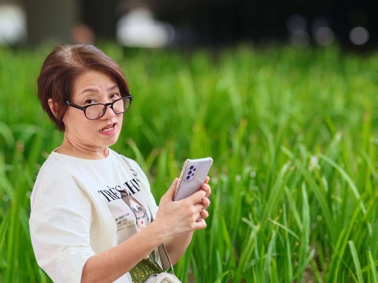 Portrait of a learner holding her smartphone in front of a wall of tall green leaves rendered as soft bokeh