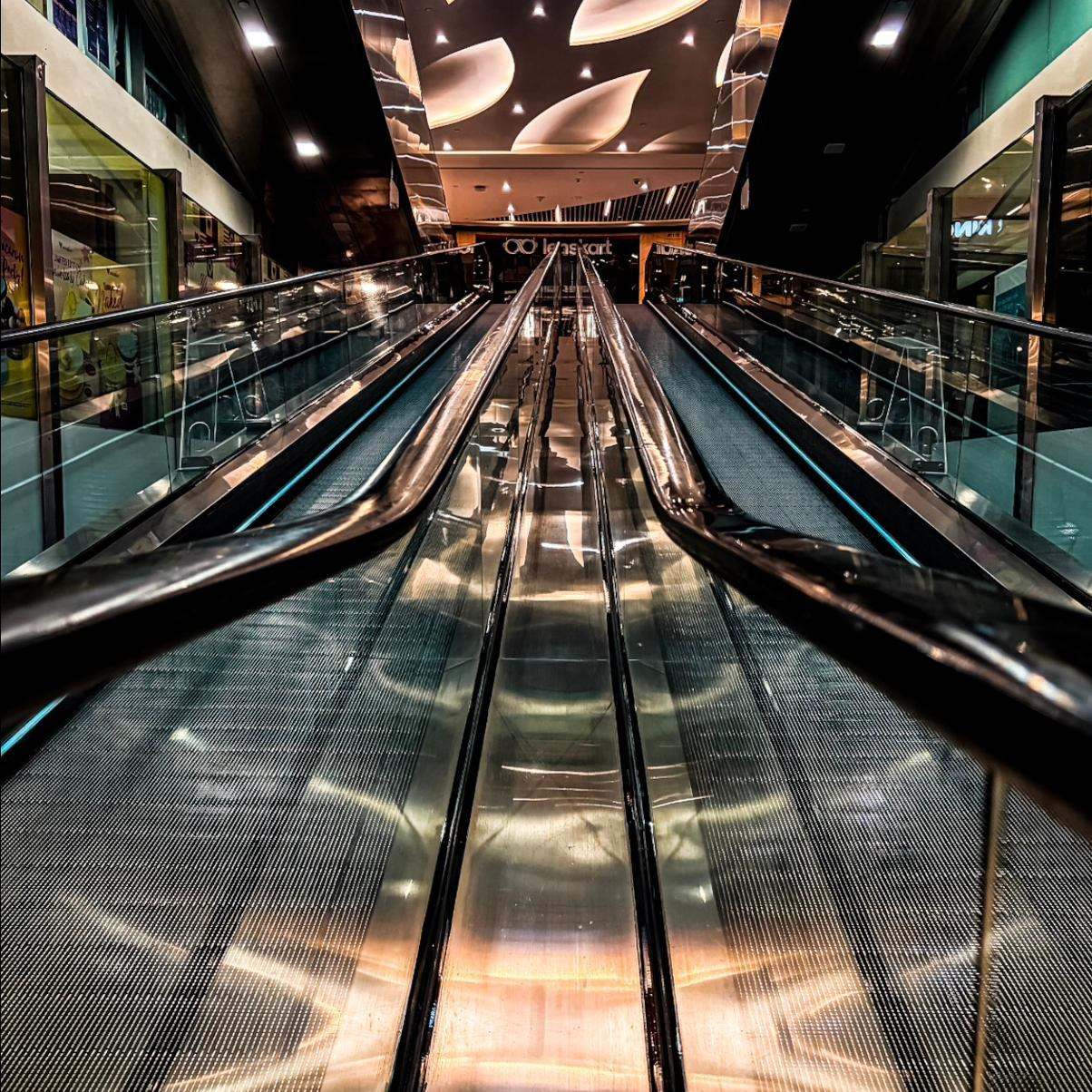 Night shot of twin mall travelators converging toward a vanishing point under a sculpted ceiling, taken on a smartphone